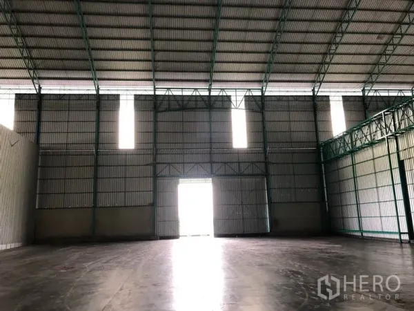Warehouse for rent in Sai Noi, Nonthaburi - Interior with high steel truss ceiling, corrugated walls and a bright central access door.