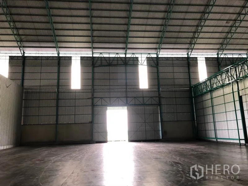 Warehouse for rent in Sai Noi, Nonthaburi - Interior with high steel truss ceiling, corrugated walls and a bright central access door.