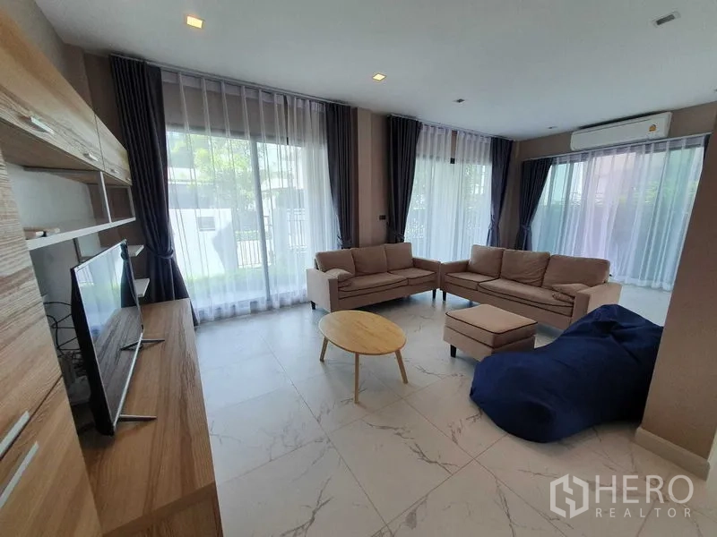 Detached House for rent in Khlong Luang, Pathum Thani - Open living area with two sofas, ottoman, bean bag and full-height windows.