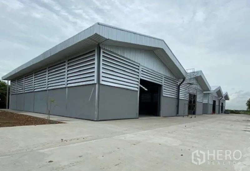 工厂 出租在Pathum Thani - 位于Lat Lum Kaeo的现代灰色钢结构工厂，山墙屋顶与百叶通风墙，前方为宽阔混凝土装卸场。