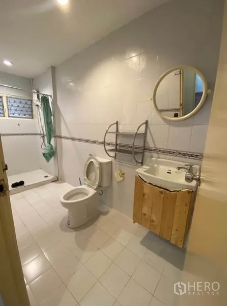 Townhouse for rent in Khlong Toei, Bangkok - Spacious bathroom with shower zone, toilet, vanity, and round mirror on white tiles.