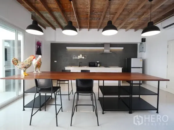 Townhouse for rent in Khlong Toei, Bangkok - Open-plan townhouse kitchen in Phra Khanong, Bangkok with long wooden dining table, pendant lights, exposed timber ceiling and modern appliances.