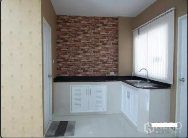 Home Office for rent in Bueng Kum, Bangkok - Compact pantry kitchen with white cabinets, black countertop, brick feature wall and corner sink.