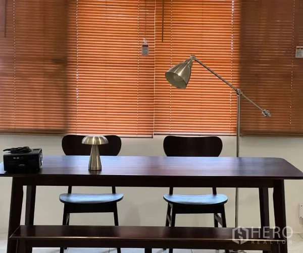 Townhouse for rent - Dining table set with two chairs and task lamp against timber blinds.