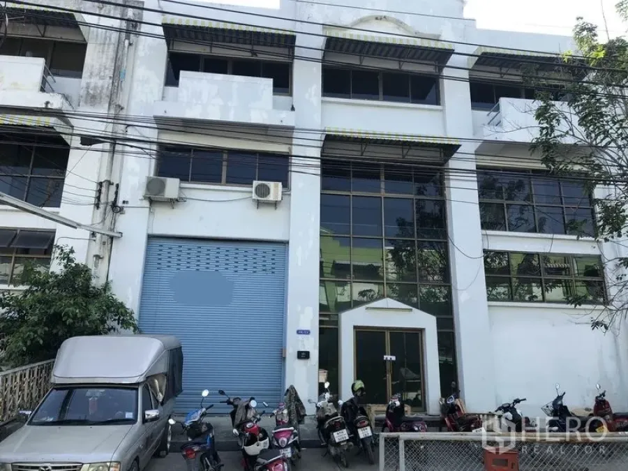 工厂 出租在Bang Sao Thong, Samut Prakan - 工厂外立面，蓝色卷帘门与高挑玻璃门面，机车停放区。