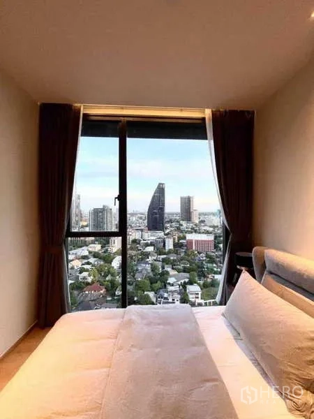 Condominium for rent or sale in Khlong Toei, Bangkok - Cozy bedroom with floor-to-ceiling window showcasing Bangkok skyline views.