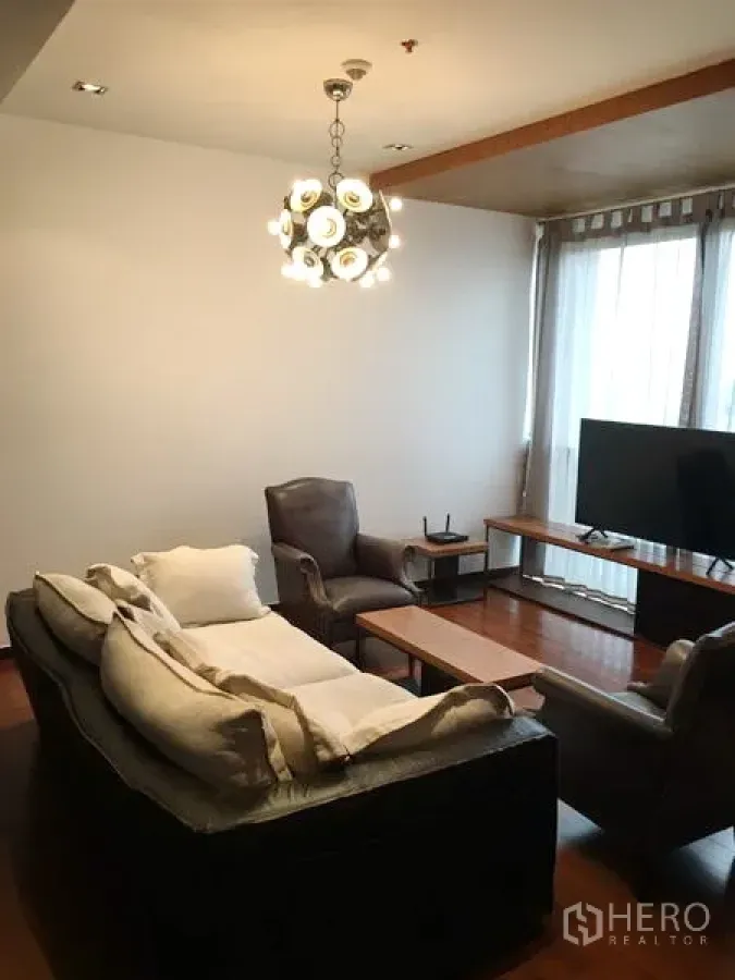 Condominium for rent or sale in Khlong Toei, Bangkok - Khlong Toei condo living room with leather sofa, armchairs, TV and modern pendant light.