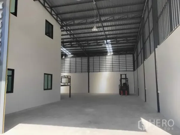 Factory for rent in Lam Luk Ka, Pathum Thani - High-ceiling warehouse floor with hanging lights and space for forklift beside office wing.