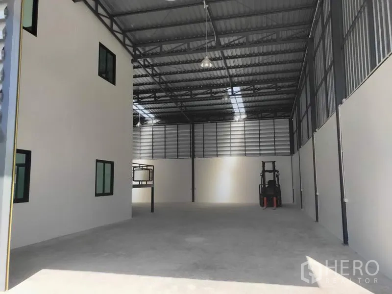 Factory for rent in Lam Luk Ka, Pathum Thani - High-ceiling warehouse floor with hanging lights and space for forklift beside office wing.