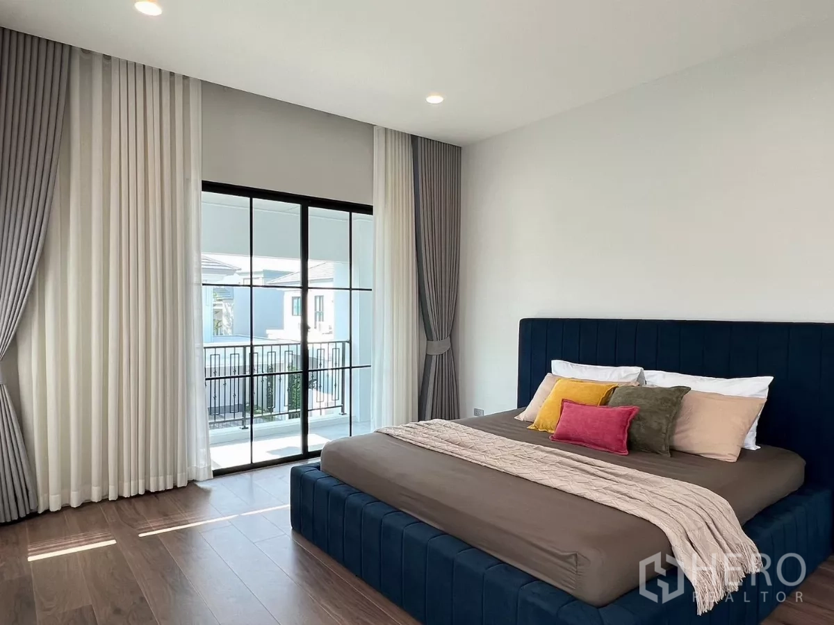 Detached House for rent in Khan Na Yao, Bangkok - Primary bedroom with navy upholstered bed and sliding doors to a private balcony.