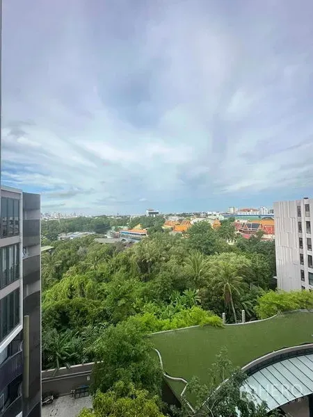 Condominium for sale in Watthana, Bangkok - High‑floor view between two condominium buildings across a treetop canopy and temple roofs under a wide sky.