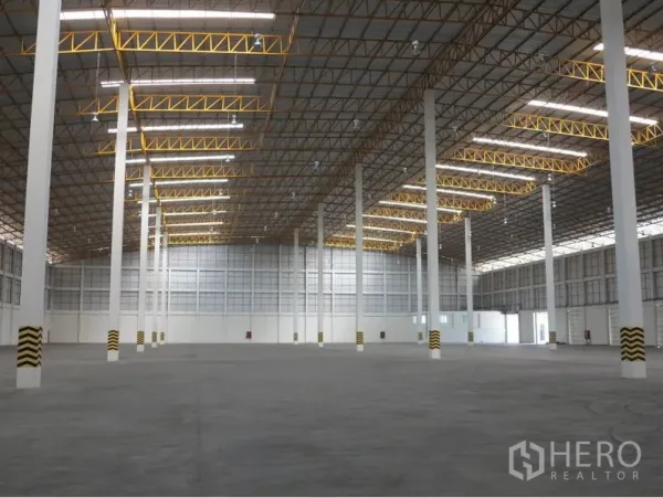 Warehouse for rent in Lopburi - Spacious warehouse interior with high ceiling, white columns and yellow steel trusses