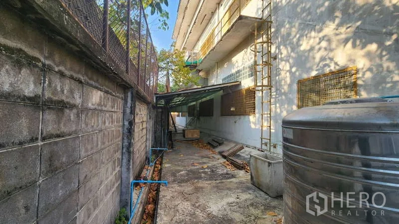 Factory for rent in Chom Thong, Bangkok - Side service lane with water tank, utility pipes and perimeter fence.