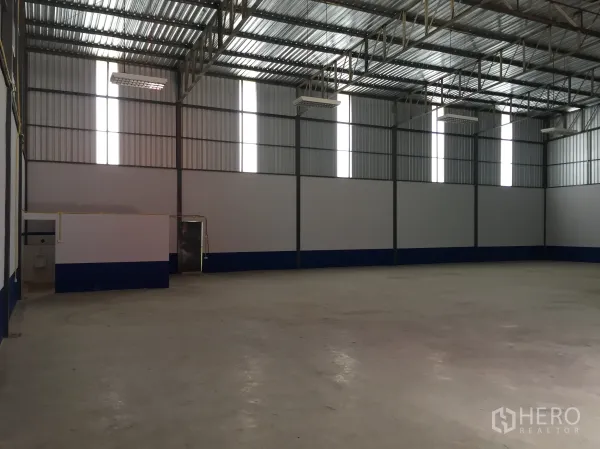 货栈 出租在Lam Luk Ka, Pathum Thani - 空置仓库内部，高钢结构屋顶、混凝土地面、纵向采光窗，角落带卫生间和小办公室。