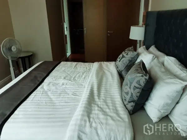 Condominium for rent or sale in Khlong Toei, Bangkok - Primary bedroom looking toward the ensuite door, large bed with patterned cushions.