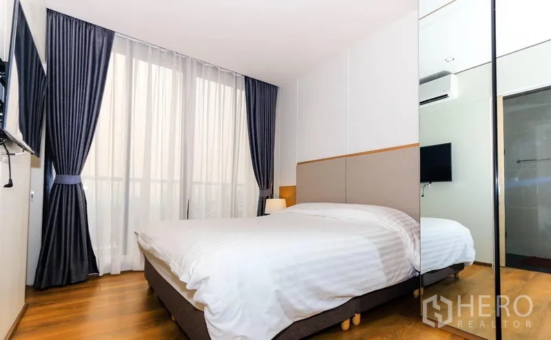 Condominium for rent in Khlong Toei, Bangkok - Bright bedroom with double bed, mirrored wardrobe and floor-to-ceiling window drapes.