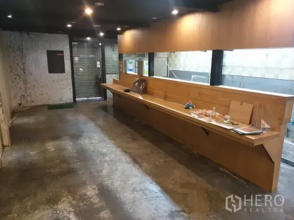 店屋 出租在Khlong Toei, Bangkok - 一层空间设长木吧台、水泥地面与玻璃卷闸门。