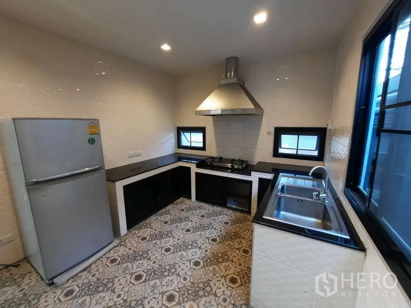 Home Office for rent in Huai Khwang, Bangkok - Fitted kitchen with L-shaped black countertops, gas hob, range hood and patterned floor tiles.