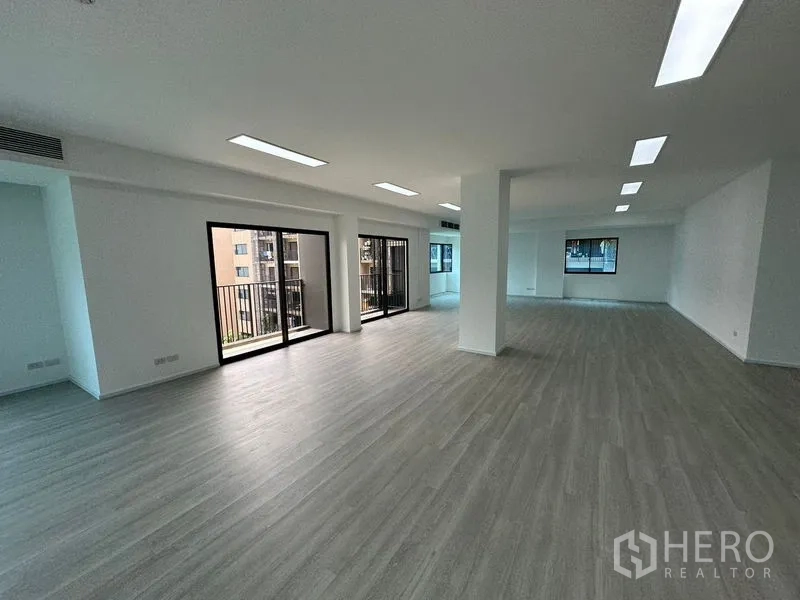 Office Space for rent - Bright office interior showing two sliding glass doors with balcony railings, a central column and long room under recessed LED lights.