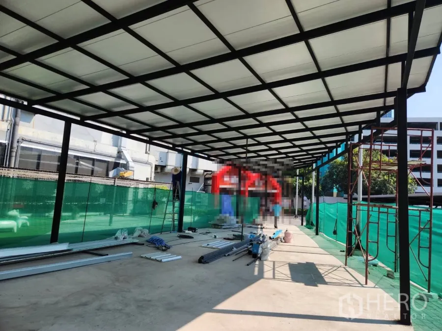 Retail Space for rent in Khlong Toei, Bangkok - Open-air retail pavilion with steel frame and translucent roof under construction, green safety screens and concrete floor in Khlong Toei, Bangkok.