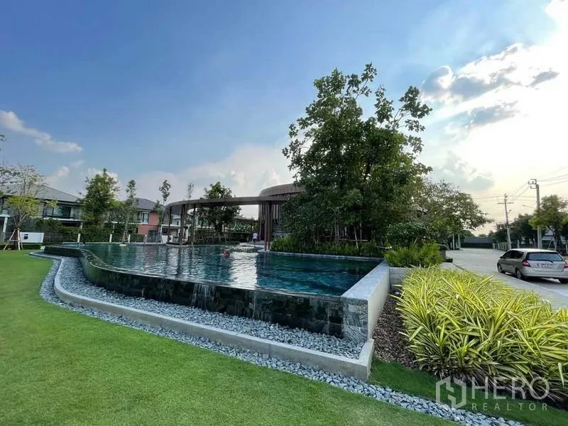 Detached House for sale in Pak Kret, Nonthaburi - Resort-style infinity-edge swimming pool beside a lawn and trees within the estate.