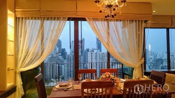 Condominium for rent in Khlong Toei, Bangkok - Dining space by wide sliding doors opening to balcony with Bangkok skyline view.