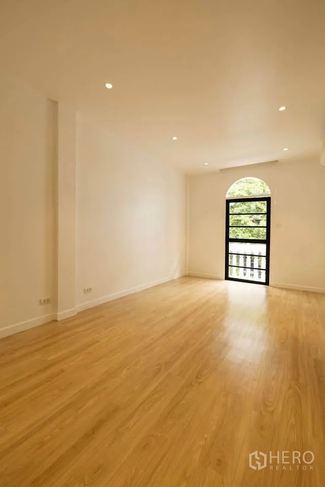 Townhouse for rent in Khlong Toei, Bangkok - Expansive room with arched doorway opening to a balcony with green views.