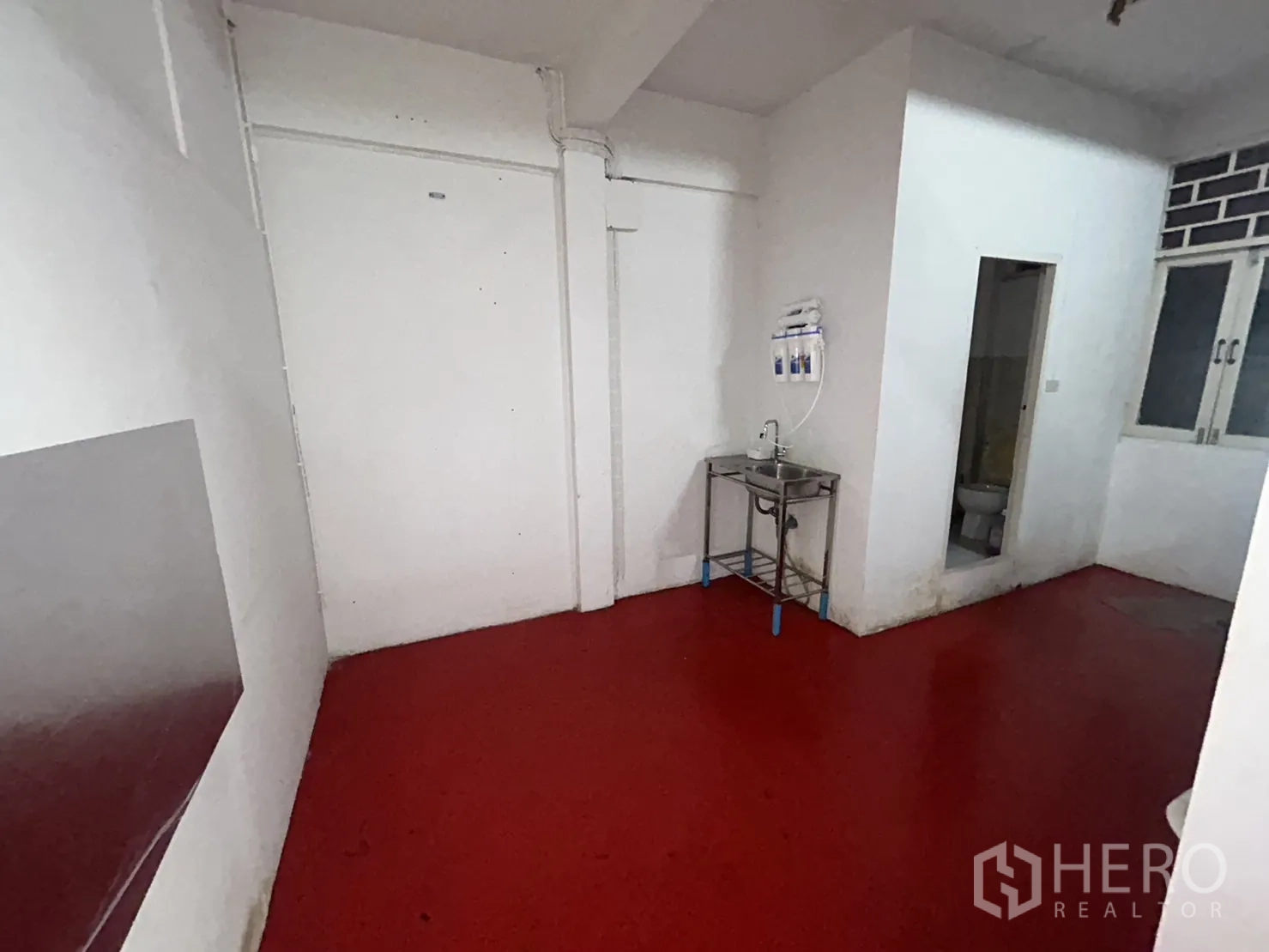 Shophouse for rent in Khlong Toei, Bangkok - Back prep area with stainless sink, red epoxy floor, and doorway to a restroom.