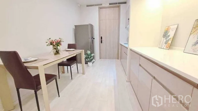 Condominium for sale in Pathum Wan, Bangkok - Dining nook with two-seat table beside a long storage counter and upper cabinets on light wood floors.