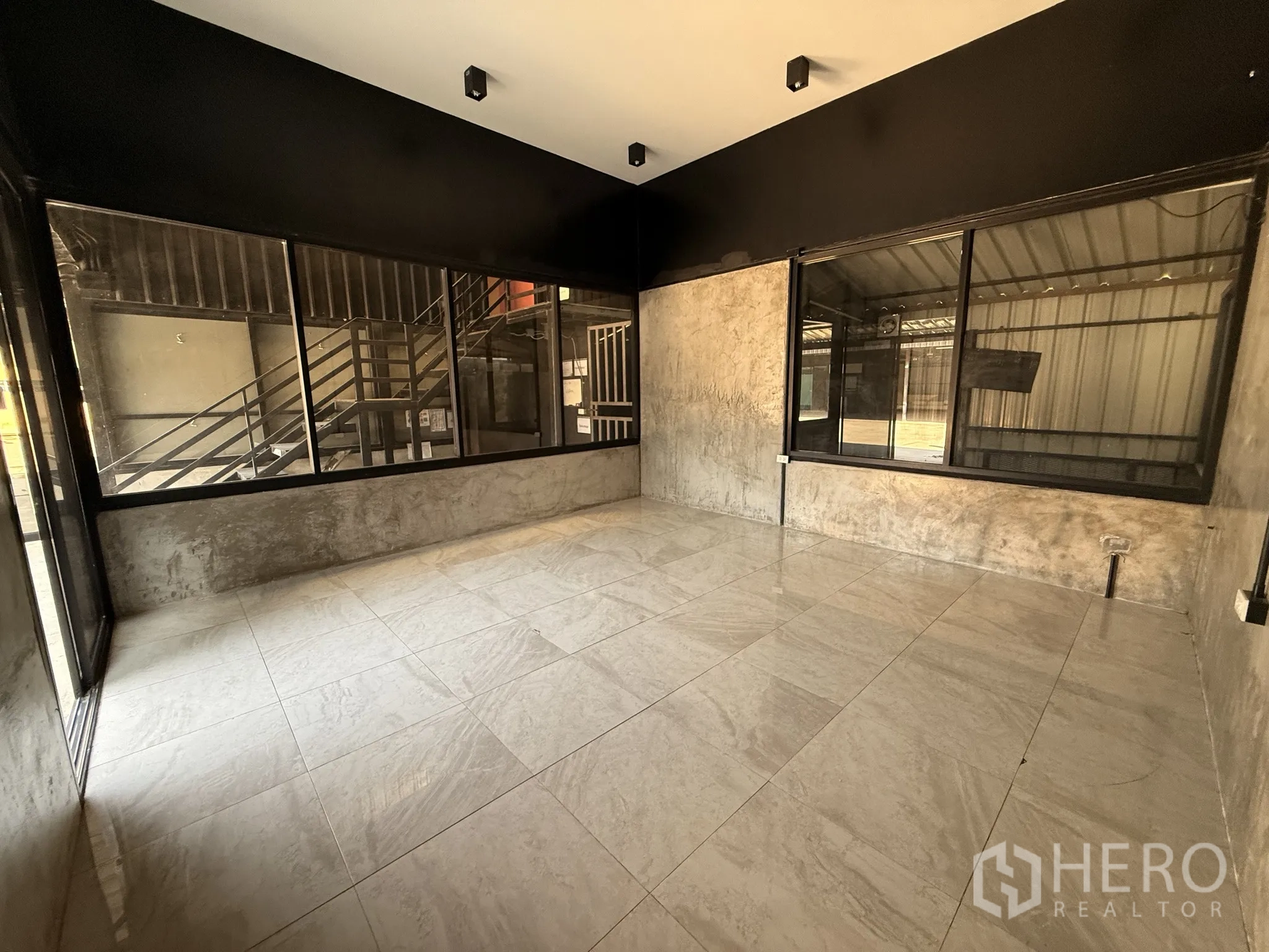 Warehouse for rent in Lat Krabang, Bangkok - Ground-floor office room with large windows, light tiles, and a view of the exterior metal staircase.
