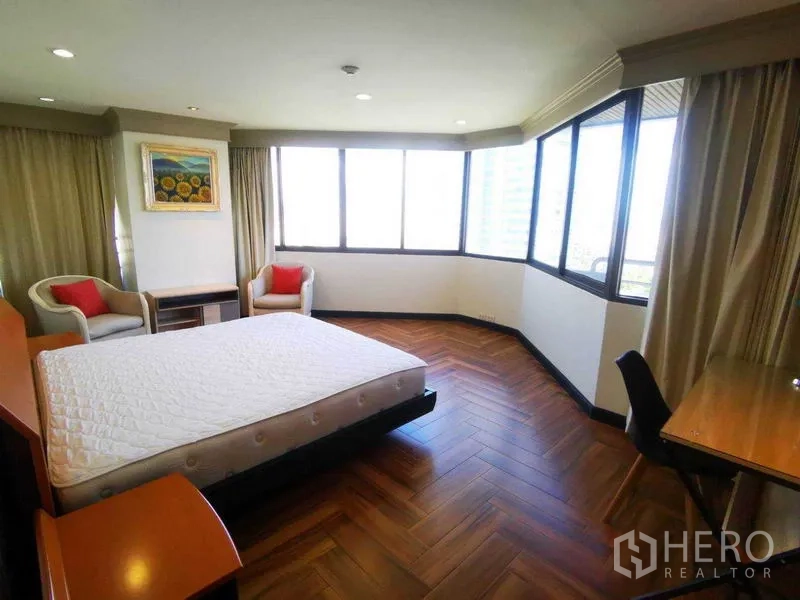 Condominium for rent in Khlong Toei, Bangkok - Corner bedroom with wraparound windows, seating area and herringbone wood floor.