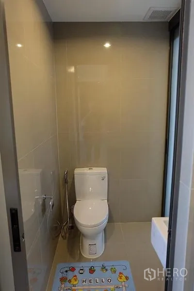 Condominium for rent in Khlong Toei, Bangkok - Compact bathroom with beige tiles, modern toilet and bidet spray beside a glass door.
