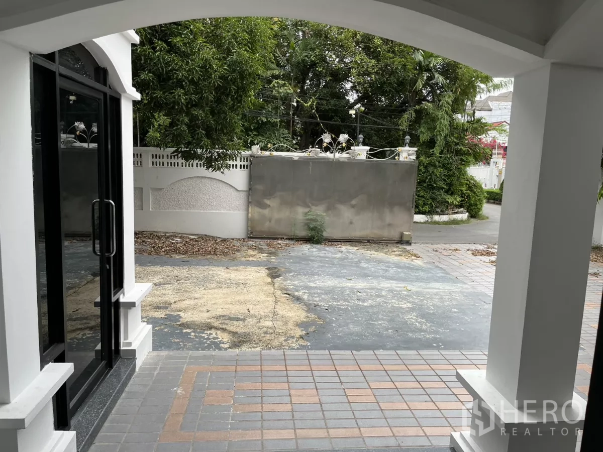 独立式住宅 出租在Watthana, Bangkok - 从有顶门廊望向大门与铺砖庭院，周围绿树成荫。
