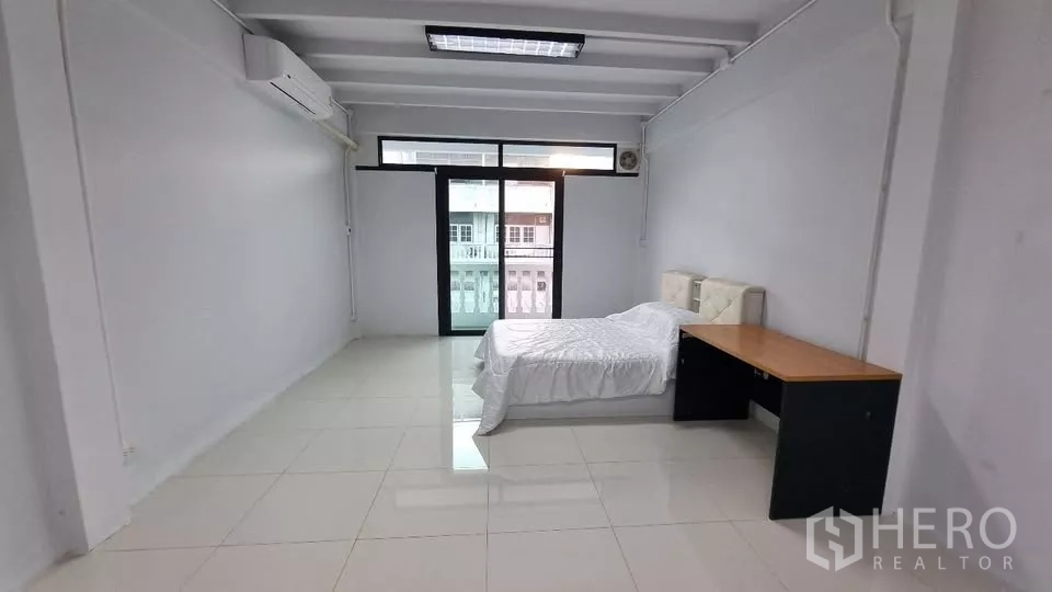 Townhouse for rent in Huai Khwang, Bangkok - Bedroom with sliding doors to a balcony and ample natural light.