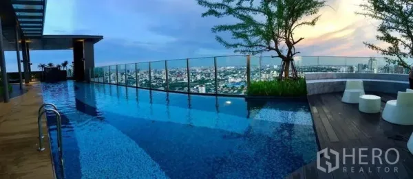 Condominium for rent in Khlong Toei, Bangkok - Rooftop infinity pool with city skyline and glass balustrade at sunset.
