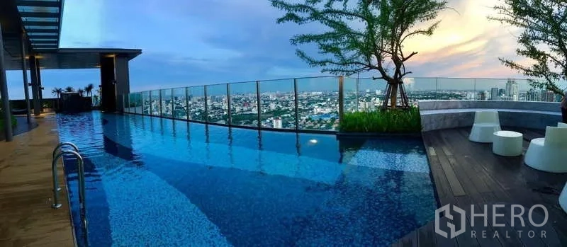 Condominium for rent in Khlong Toei, Bangkok - Rooftop infinity pool with city skyline and glass balustrade at sunset.