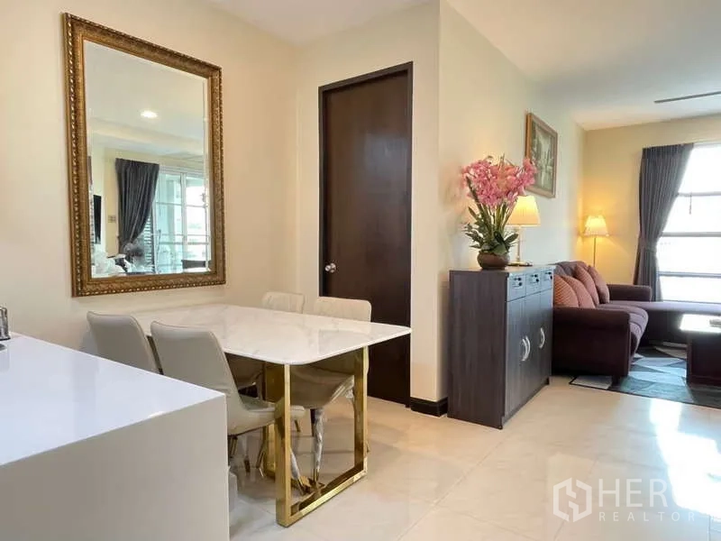 Apartment for rent in Khlong Toei, Bangkok - Dining nook with marble-top table beside living area and gold-framed mirror.