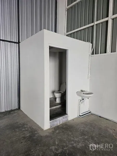 Warehouse for rent in Khlong Toei, Bangkok - Compact restroom inside the warehouse with toilet and wall-mounted sink on a concrete floor.