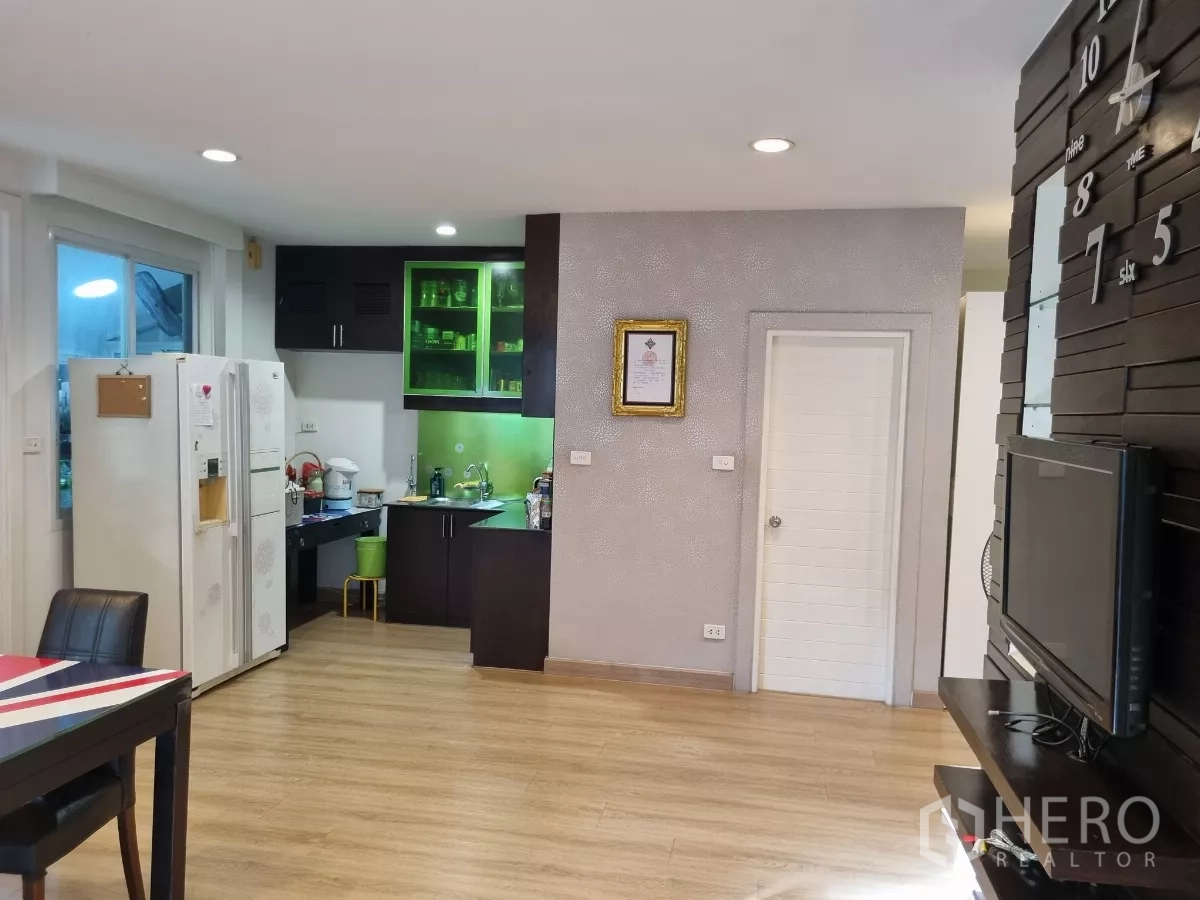 Detached House for rent in Bang Kapi, Bangkok - Open-plan kitchen with dark cabinetry, green-lit glass cupboards, and fridge.