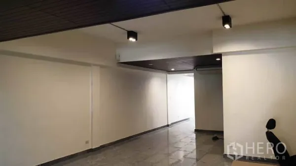 Townhouse for rent or sale in Khlong Toei, Bangkok - Long ground-floor living hall with recessed lights and polished tile flooring.