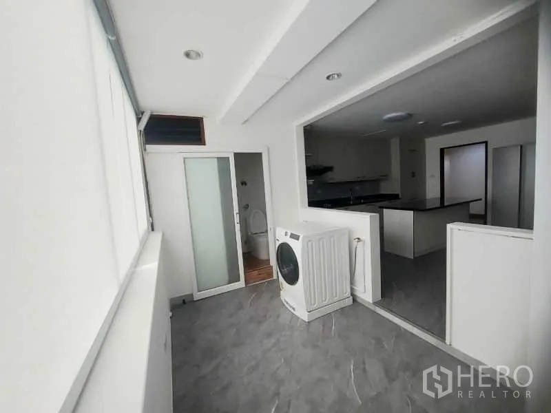 Condominium for rent in Watthana, Bangkok - Laundry area with washing machine, sliding door to utility space and gray tiled floor beside the kitchen.