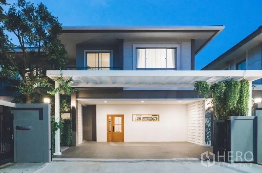 Detached House for rent - Modern two-storey house exterior at dusk with wide carport, wooden door, and landscaped greenery.
