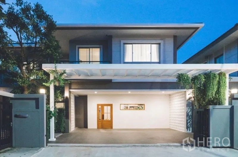 Detached House for rent - Modern two-storey house exterior at dusk with wide carport, wooden door, and landscaped greenery.