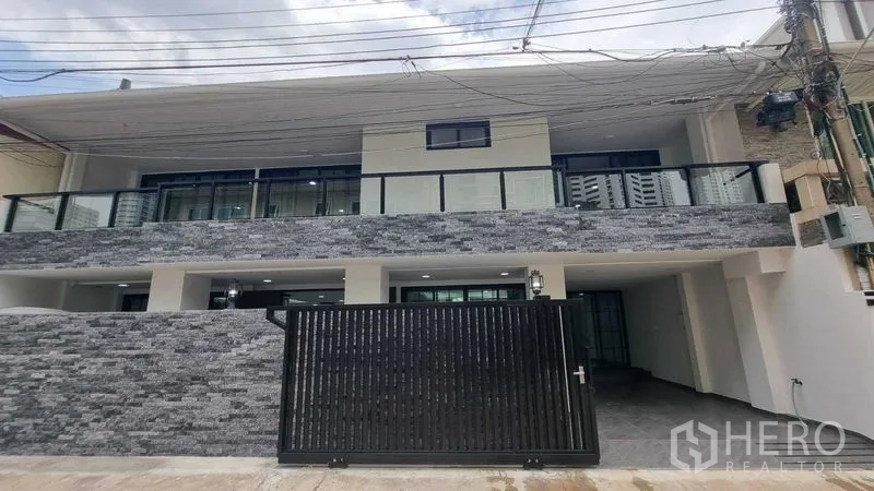 Townhouse for rent in Khlong Toei, Bangkok - Modern two-story townhouse facade with stone cladding, glass balcony, and black gate in Khlong Toei, Bangkok.