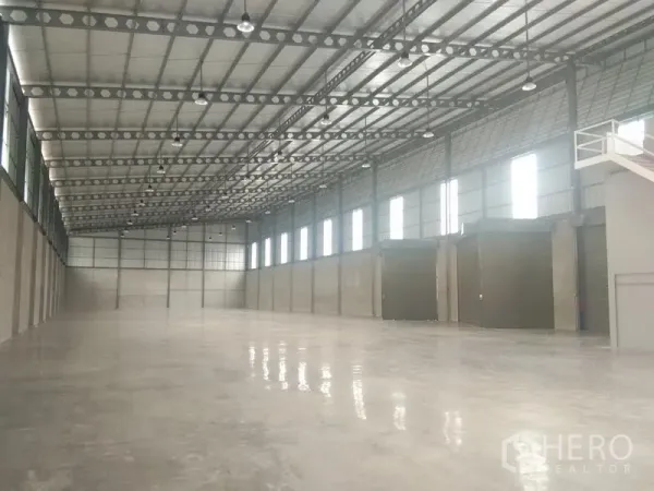 Warehouse for rent in Bang Phli, Samut Prakan - Expansive warehouse interior showing column-free space, high steel truss roof, windows for natural light, and multiple roller shutters.