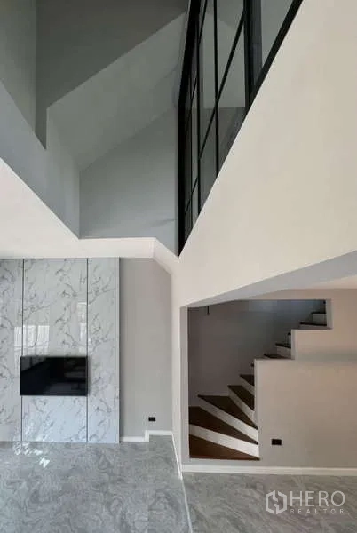 Townhouse for rent or sale in Prawet, Bangkok - View from living room showing marble TV wall and stairwell with lofted space.