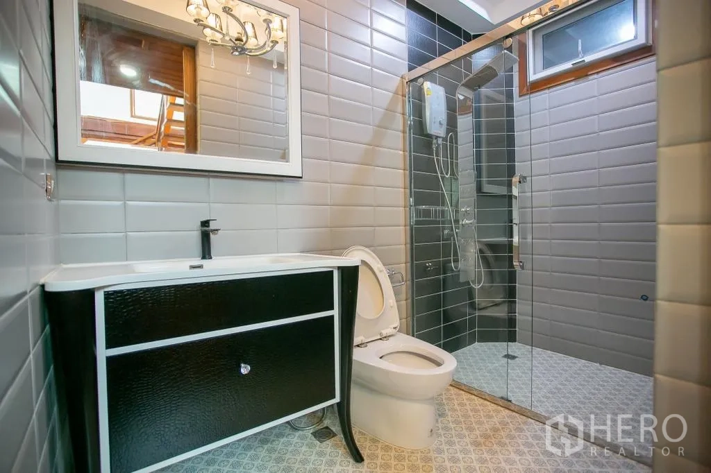 Detached House for rent or sale in Huai Khwang, Bangkok - Modern bathroom with glass shower, gray wall tiles and a black vanity.