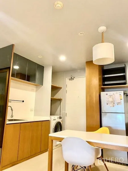Condominium for rent in Chatuchak, Bangkok - Open kitchen and dining area with wood cabinetry, white countertops, refrigerator and washing machine.