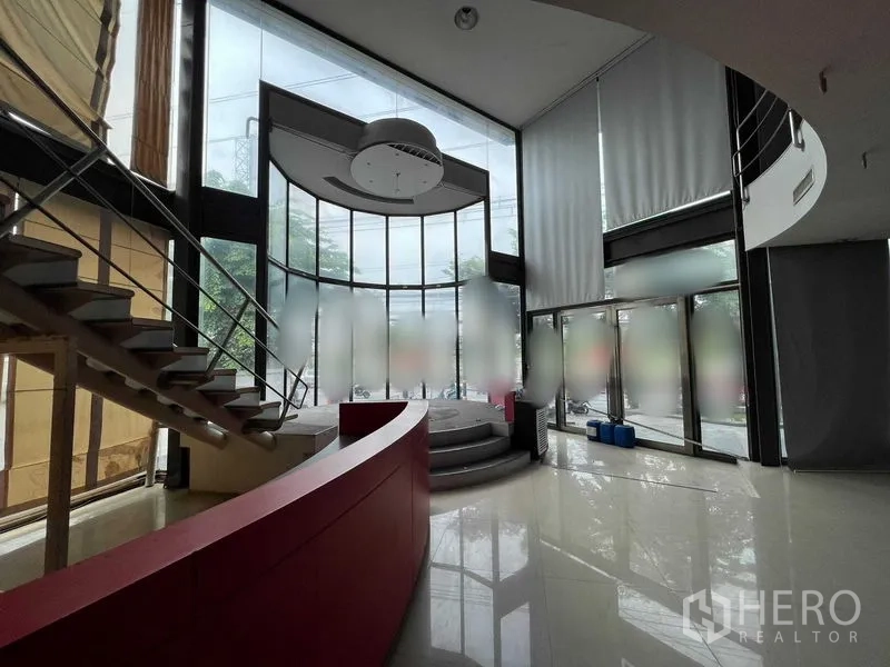 Retail Space for rent - Double-height glass atrium with curved red counter, mezzanine stairs and a raised stage.