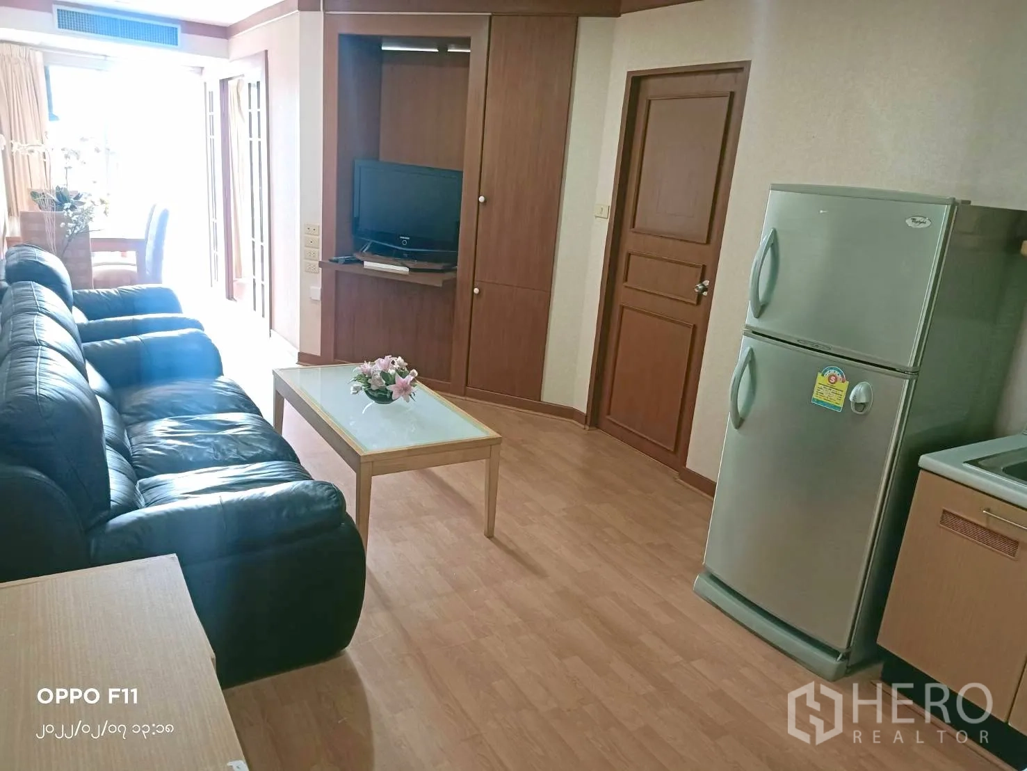 Condominium for rent in Khlong Toei, Bangkok - Bright living area with sofa, coffee table and kitchen featuring a silver refrigerator.